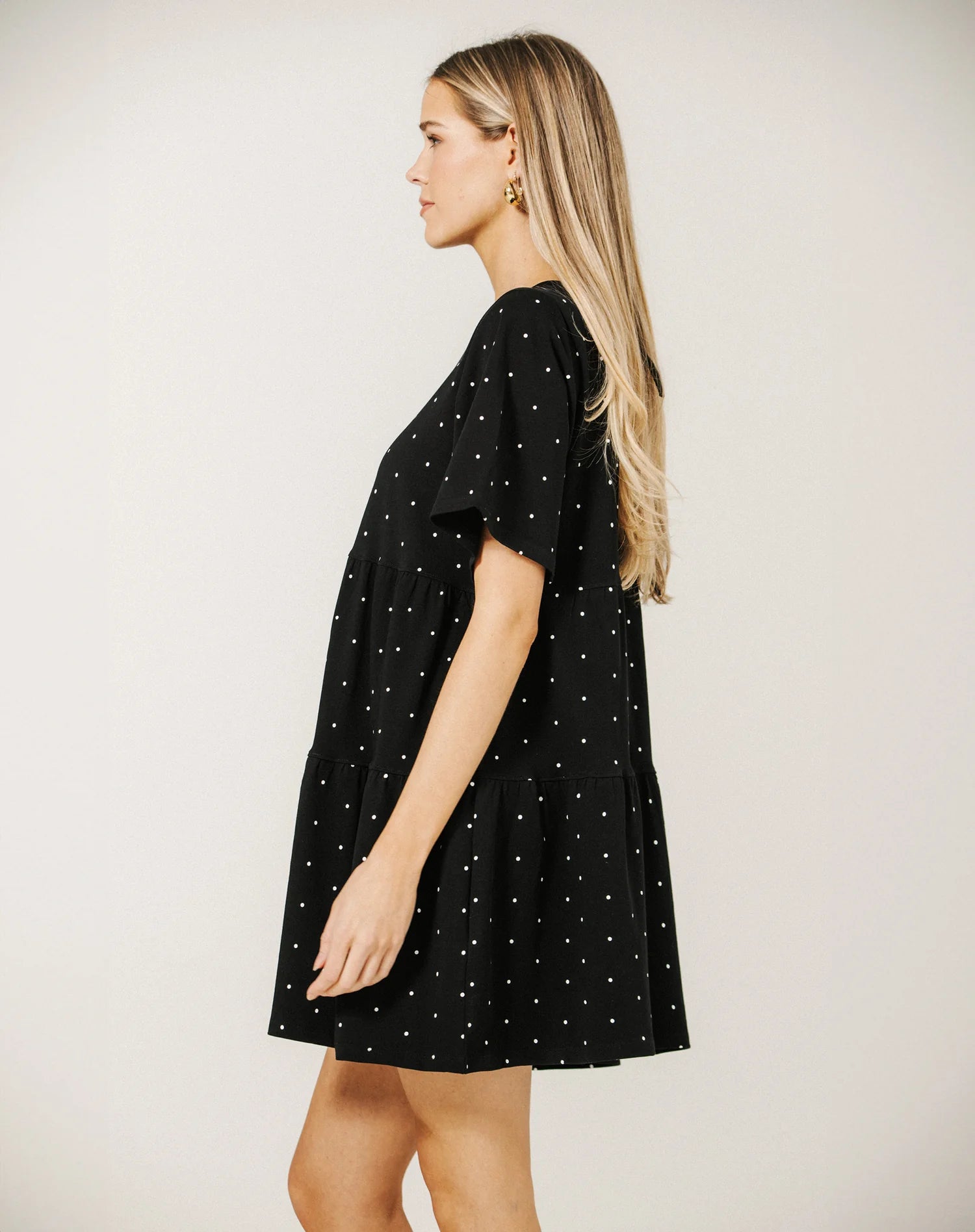 Woman wearing a black dress with white polka dots on a plain background