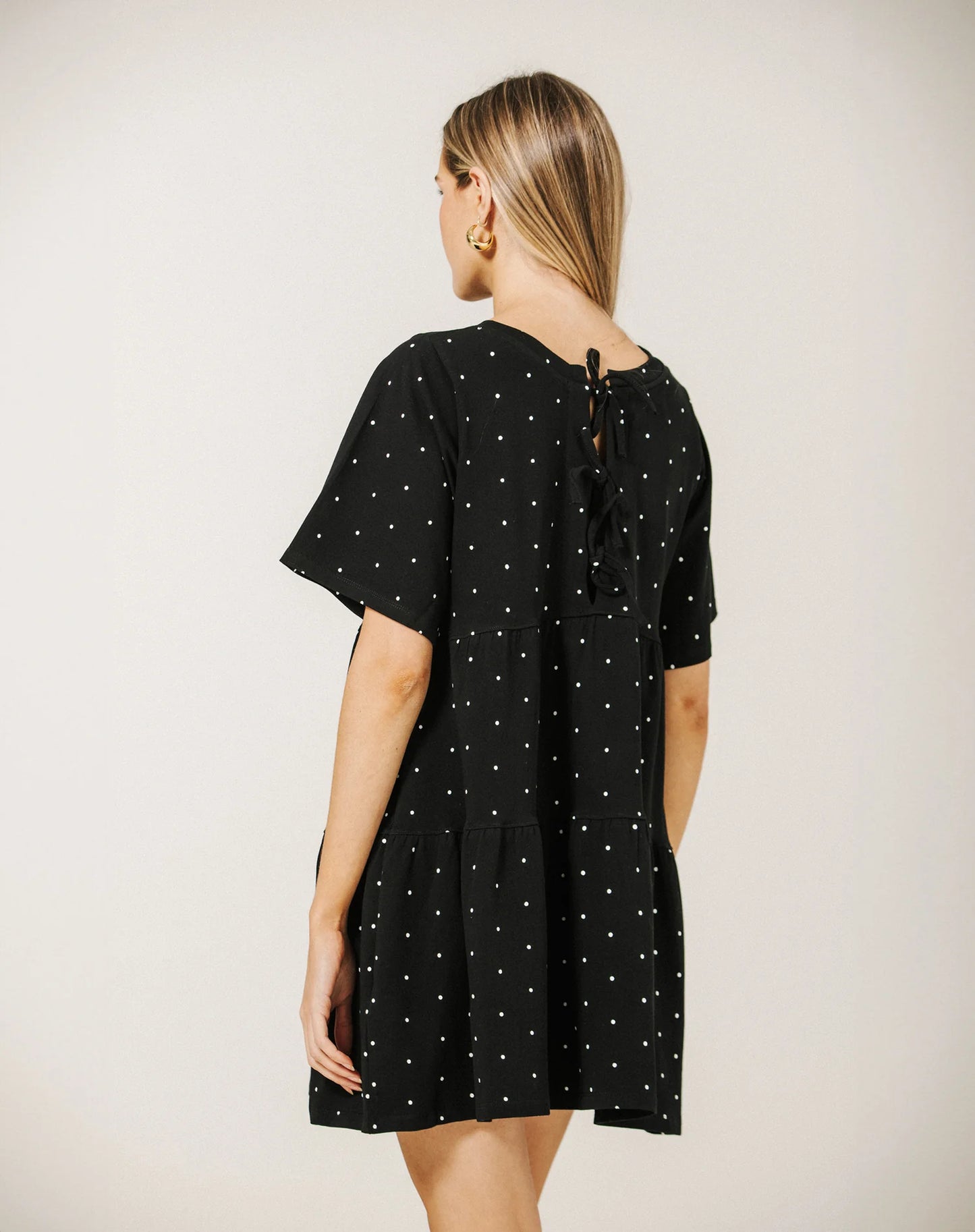 Woman wearing a black dress with white polka dots on a plain background