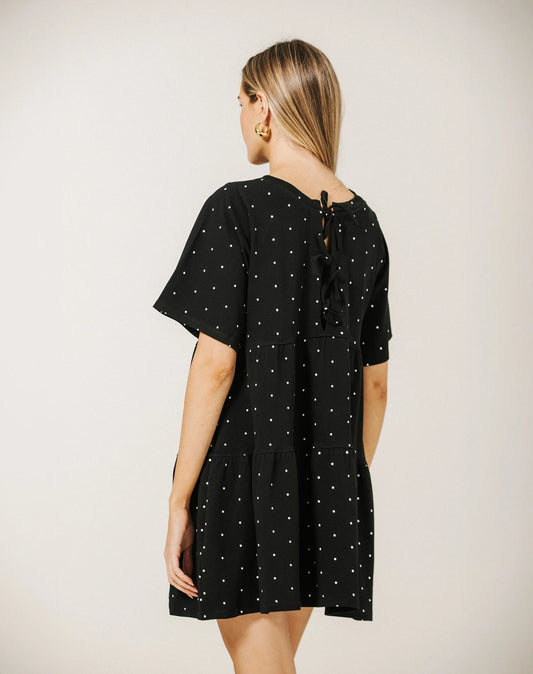 Woman wearing a black dress with white polka dots on a plain background