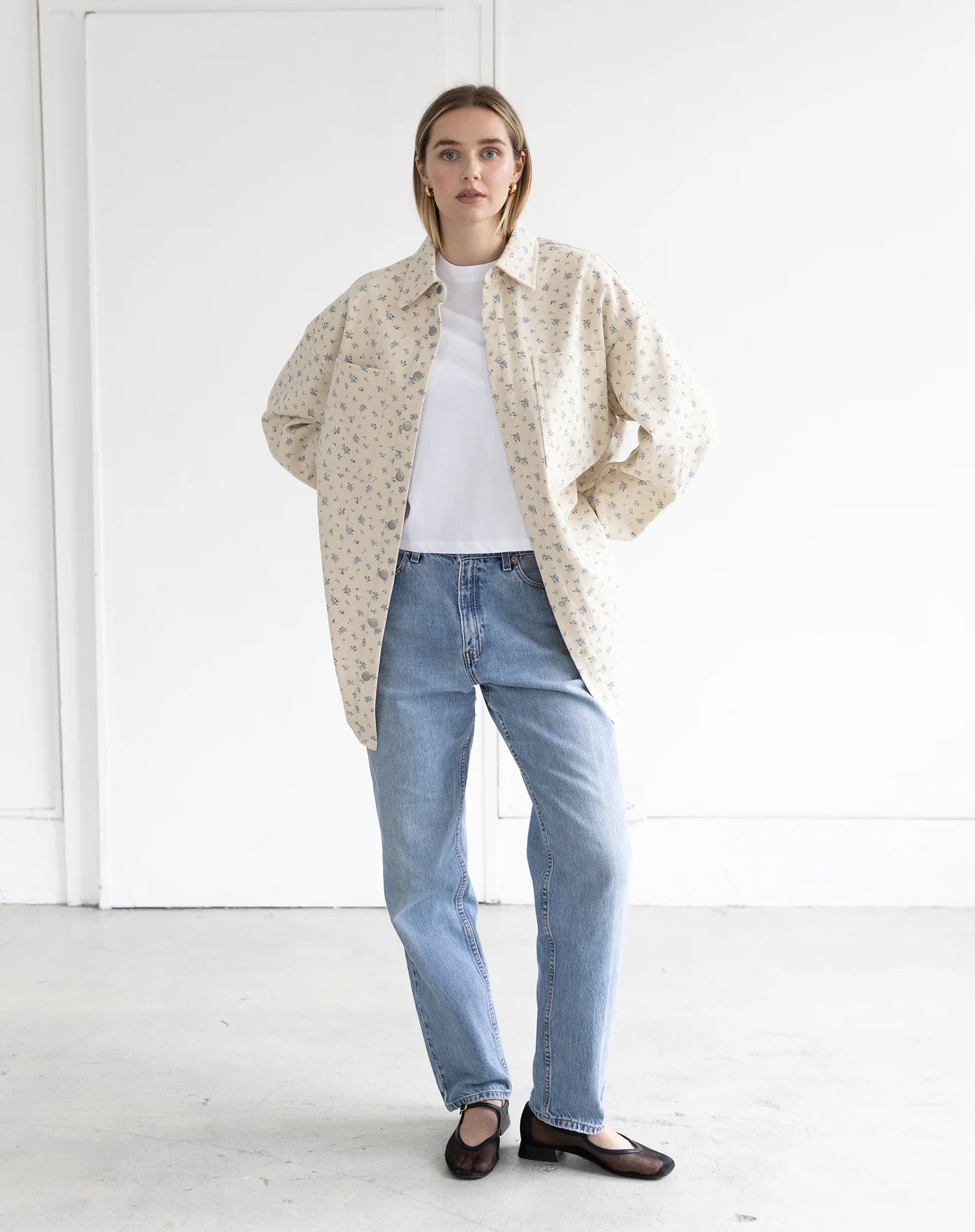 women wearing a blue floral denim jacket with blue jeans and white top on a plain background.