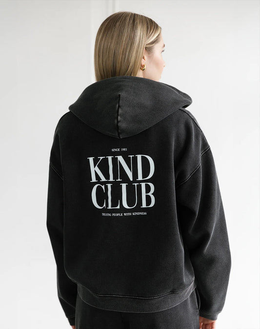 Person wearing a black hoodie with 'Kind Club' text on the back against a white background