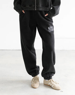 Person wearing black sweatpants with 'Kind Club' text and a black jacket on a white background