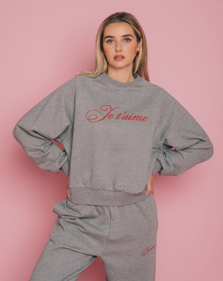 Woman wearing a gray sweatshirt and pants with 'Je t'aime' text on a pink background