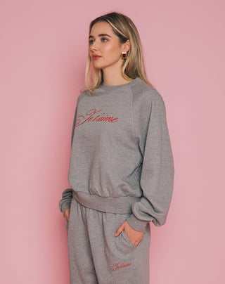 Woman wearing a gray sweatshirt with 'Je t'aime' text on a pink background