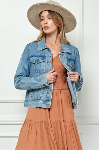 Woman wearing a denim jacket and brown dress with a beige hat against a white background