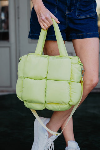 Person holding a light green quilted bag with a blurred background