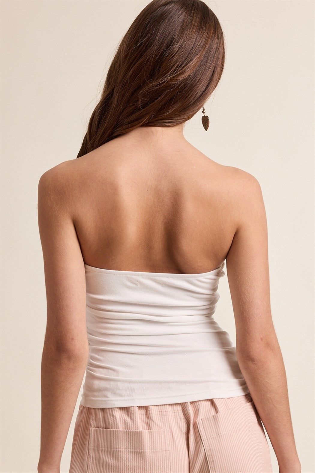 Woman wearing a white strapless top and pink pants on a beige background