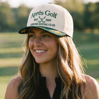 Woman wearing a cap with 'Aprés Golf' text on a blurred golf course background