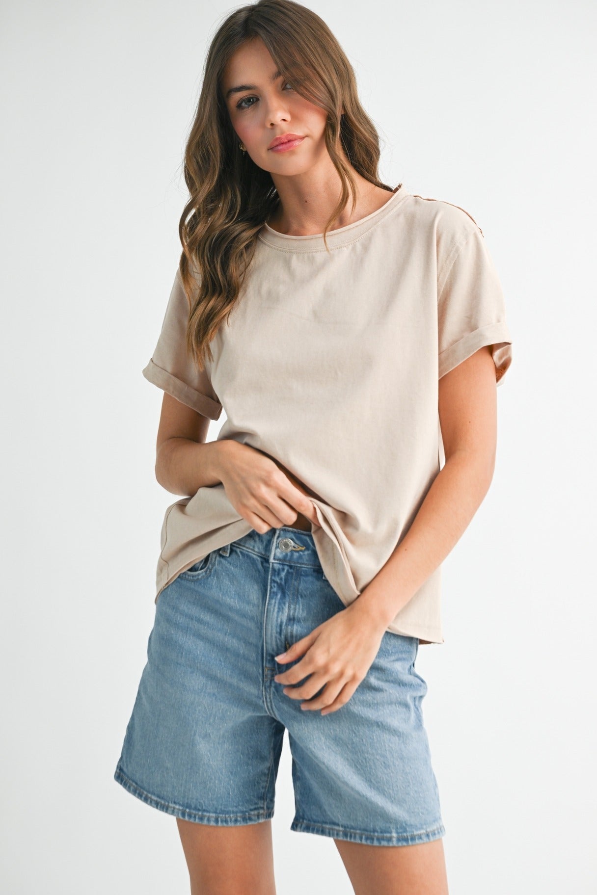 Woman wearing a beige t-shirt and blue denim shorts on a white background