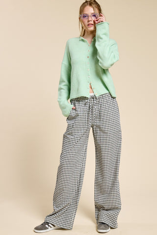 Person wearing a light green cardigan and plaid pants on a beige background