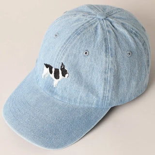 Light blue denim cap with an embroidered dog design on a beige background