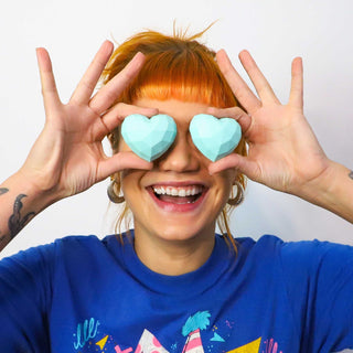 Person holding heart-shaped objects over their eyes with a blue shirt featuring graphics.