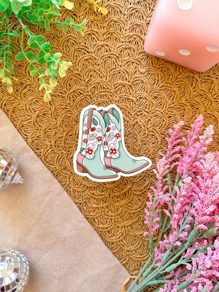 Decorative sticker of floral cowboy boots on a textured surface with flowers and a candle.