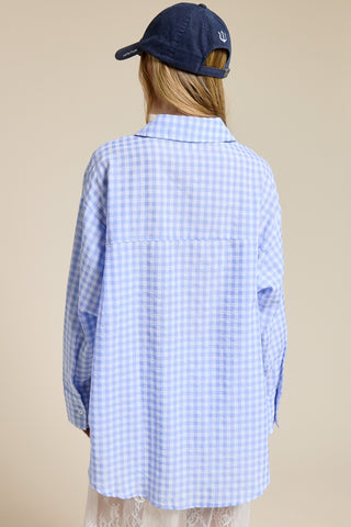 Person wearing a blue checkered shirt and navy cap on a beige background