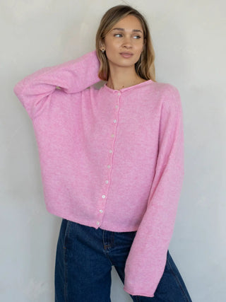 Women wearing a pink button up cardigan against a neutral background.