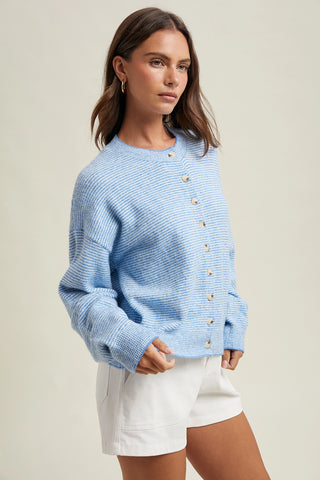 Woman wearing a blue knitted cardigan with white buttons on a beige background