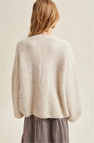 Person wearing a beige sweater and plaid pants on a plain background
