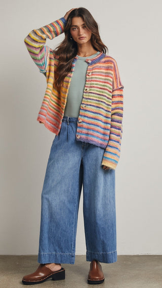 Woman wearing a colorful striped cardigan, green top, and blue jeans against a neutral background