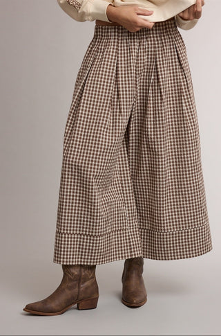 A person wearing high-waisted, wide-leg cropped pants in a brown and beige gingham pattern, styled with brown leather ankle boots and a cream top against a neutral studio background.