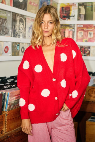 Woman wearing a red polka dot cardigan in a room with record albums on shelves.