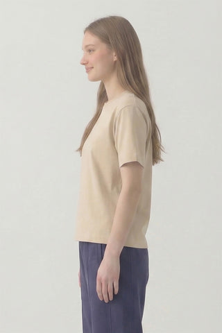 Woman wearing a beige t-shirt and purple pants against a plain background