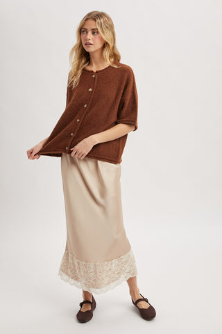 Woman wearing a brown cardigan over a beige dress with lace hem on a white background