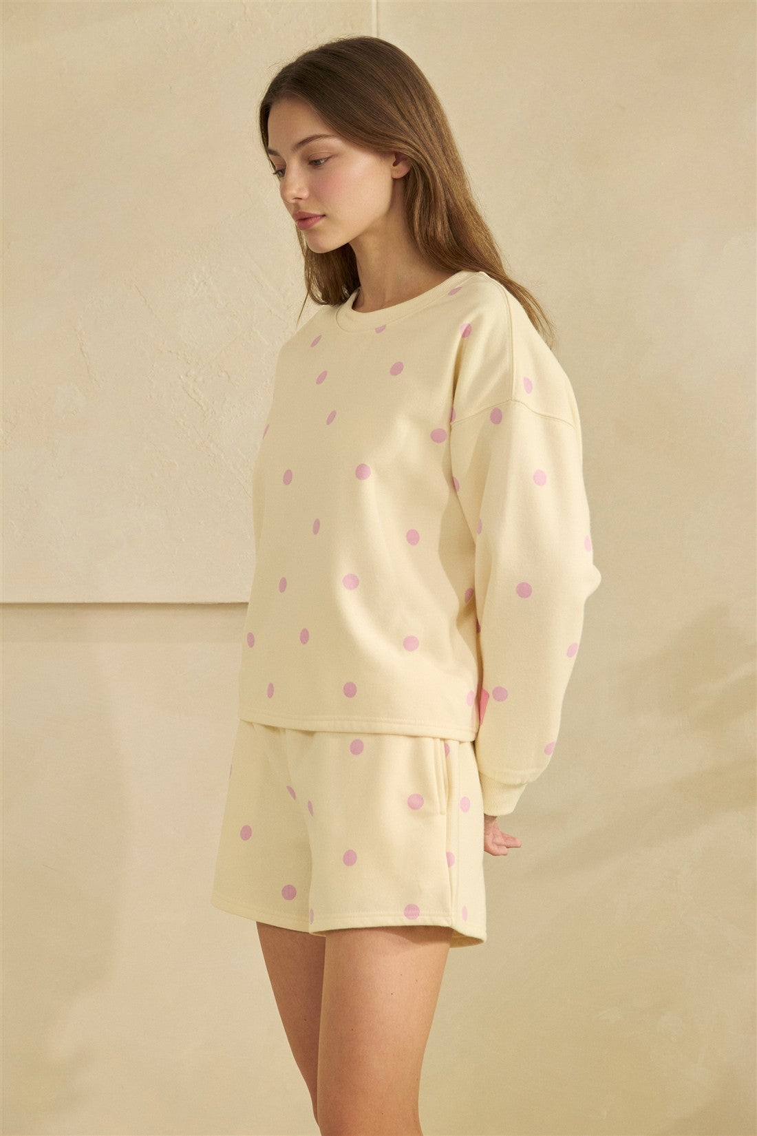 Woman wearing a light yellow pajama set with pink polka dots on a beige background