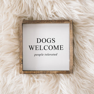Framed sign with 'DOGS WELCOME people tolerated' text on a fluffy white surface