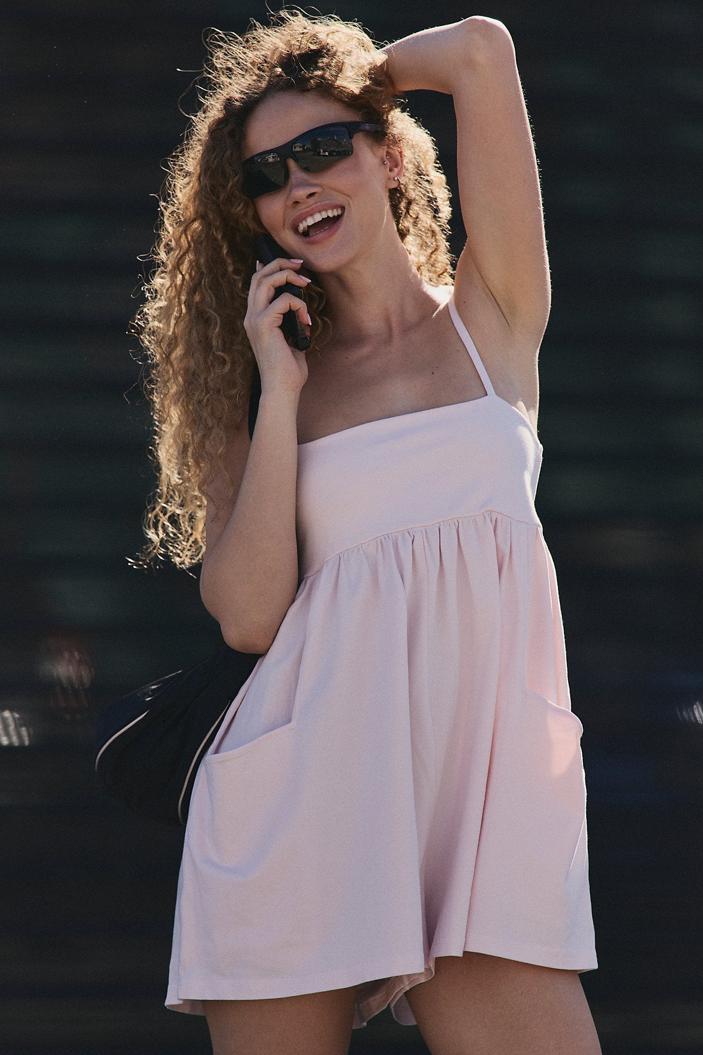 Woman in a light pink romper and sunglasses talking on a phone with a blurred background