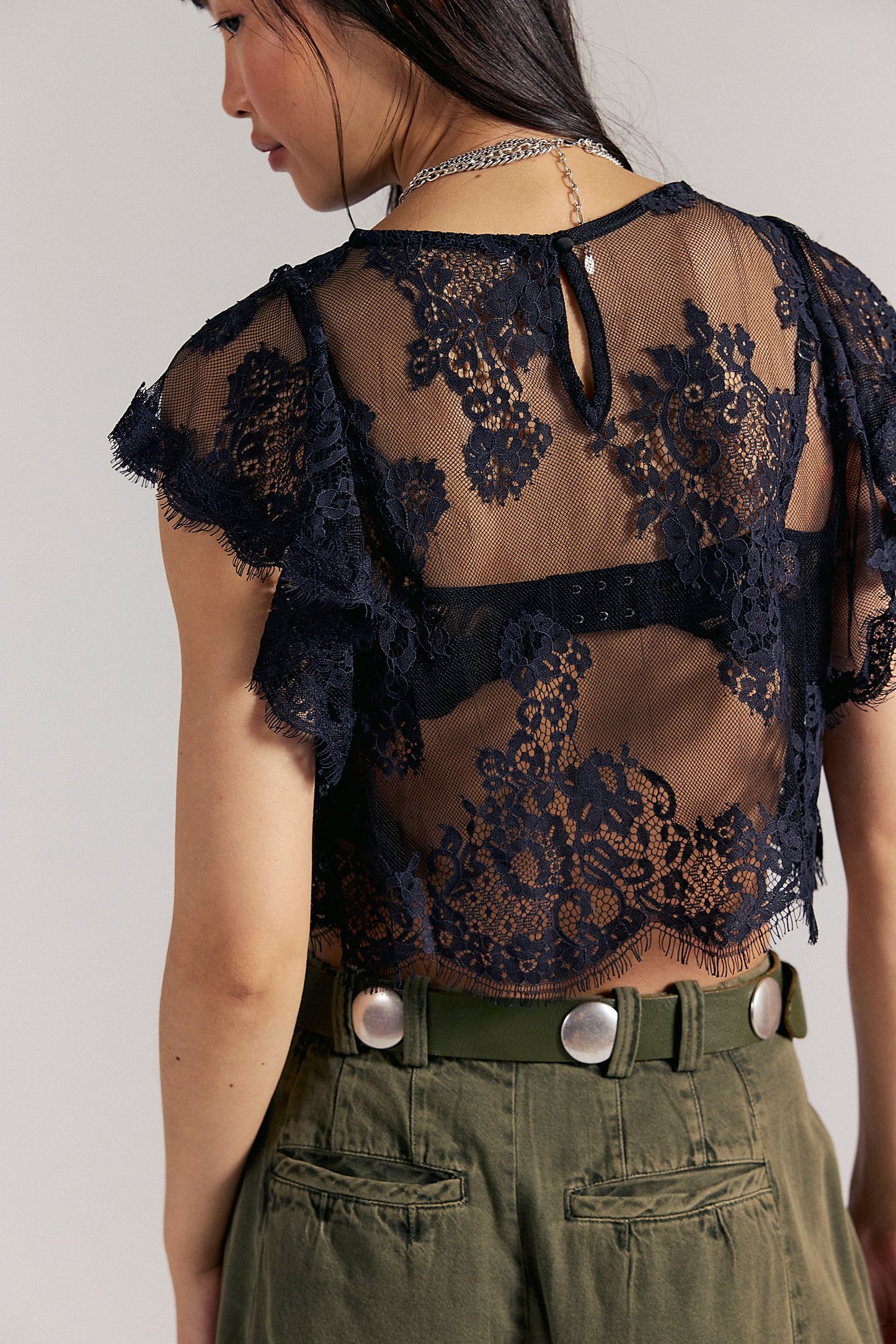 Person wearing a black lace top and green pants on a plain background