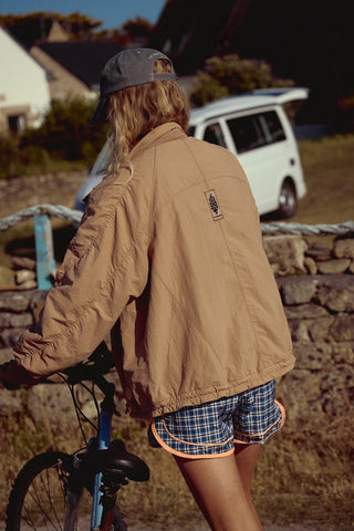 Person wearing a brown jacket and plaid shorts standing next to a bicycle with a white van in the background.