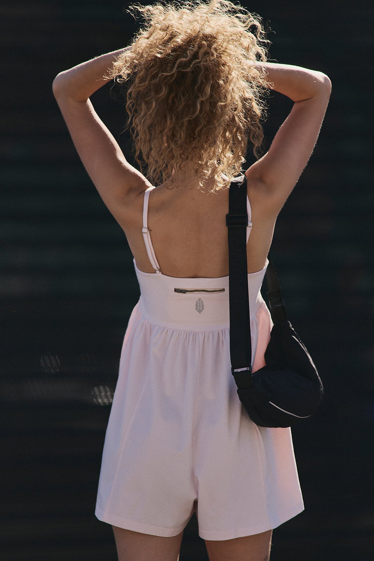 Woman in a pink romper with a black bag against a dark background