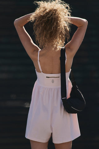 Woman in a pink romper with a black bag against a dark background
