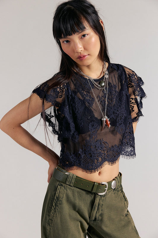 Woman wearing a black lace top and green pants against a plain background