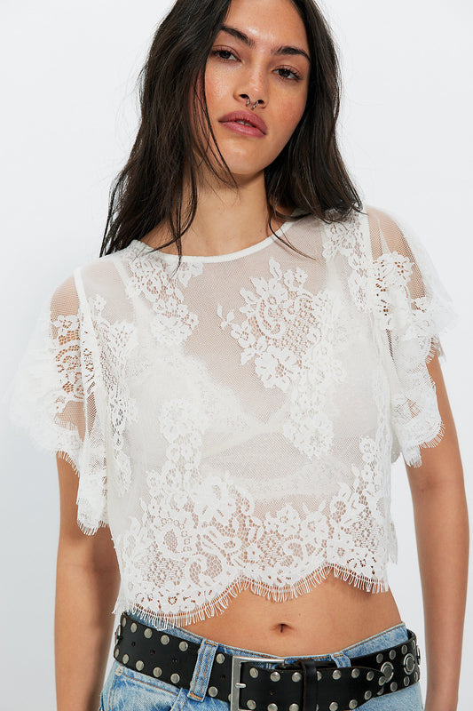 Woman wearing a white lace top with sheer sleeves on a white background