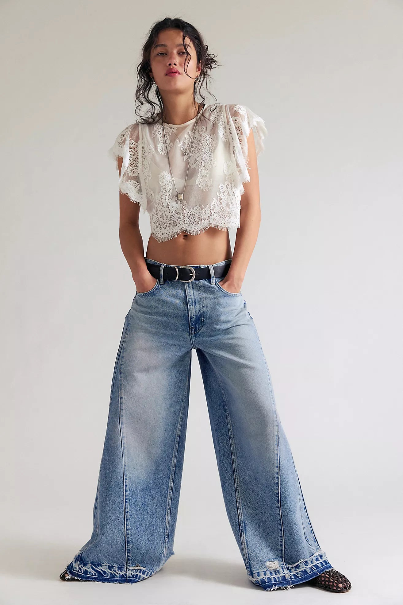 Woman wearing a white lace top and blue jeans on a plain background