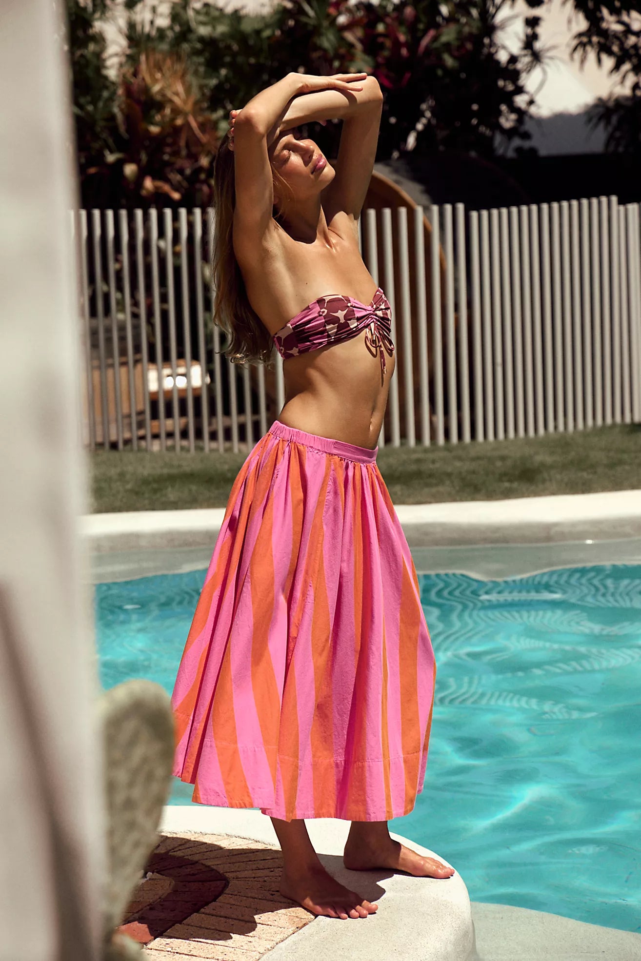 Woman in a pink and orange striped skirt standing by a pool