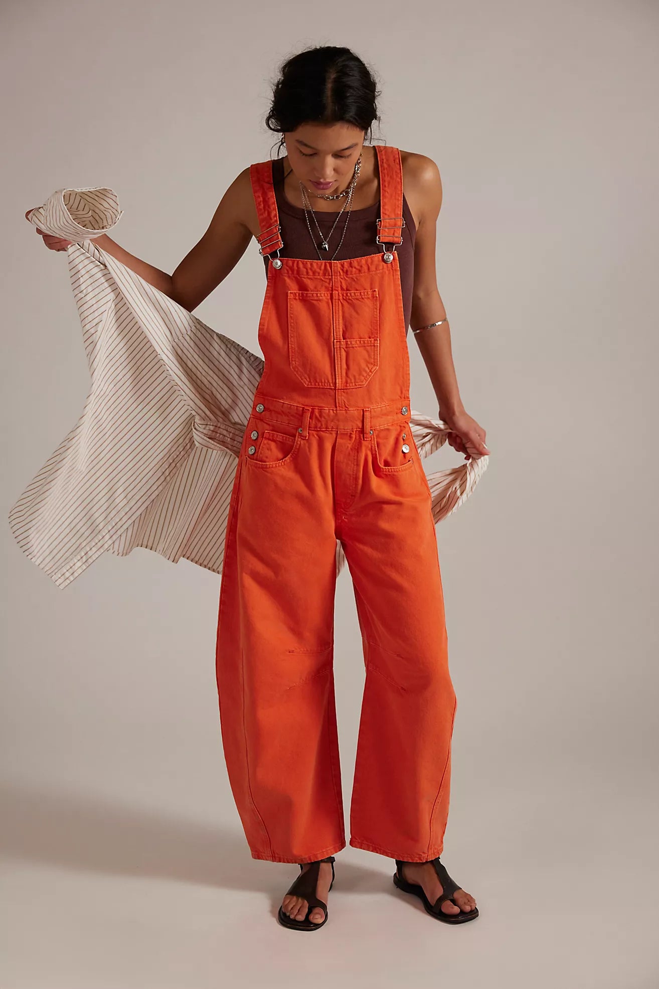 Person wearing bright orange overalls holding a striped garment against a plain background