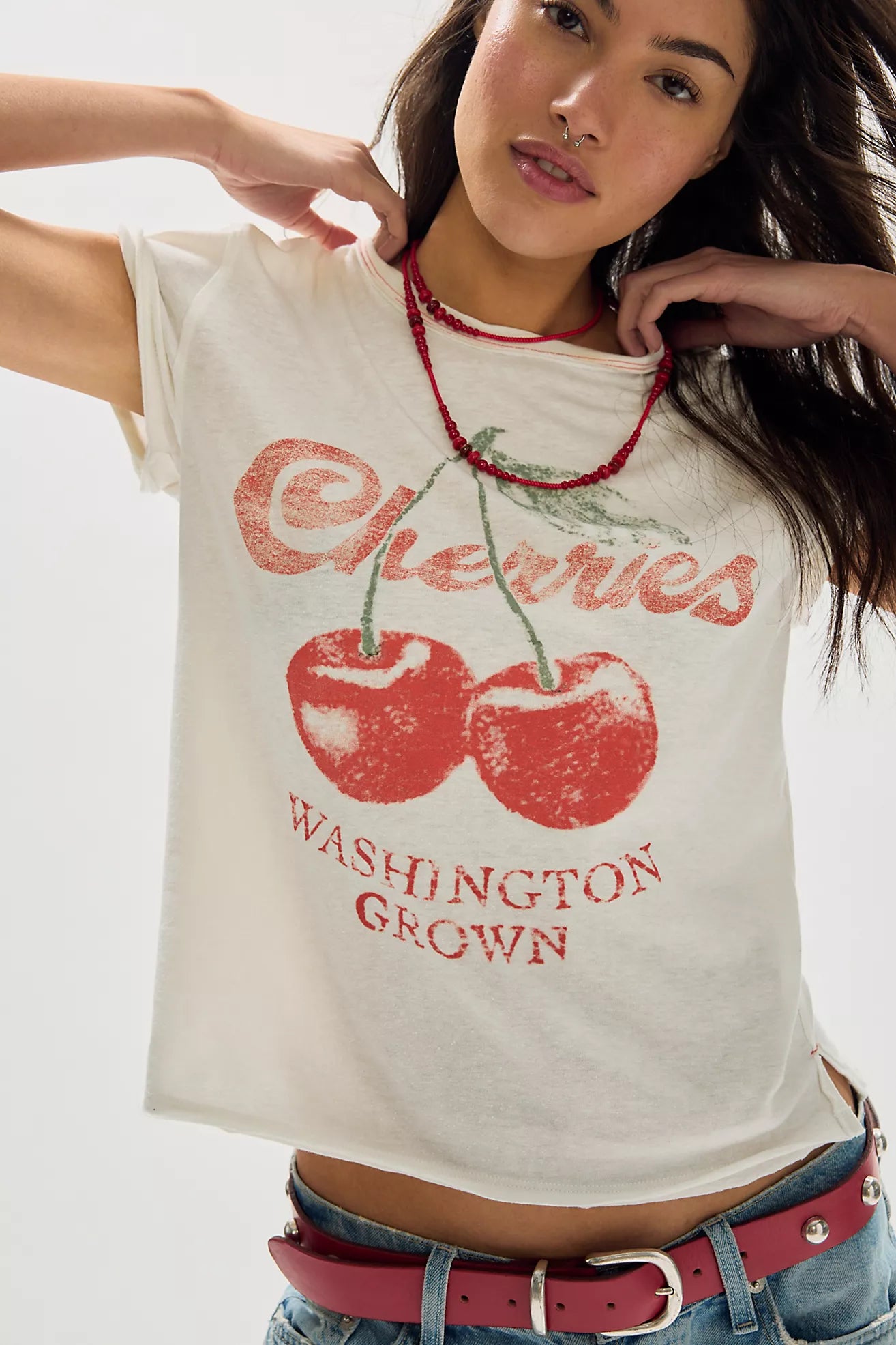 Woman wearing a white t-shirt with red cherries and 'Washington Grown' text on a plain background