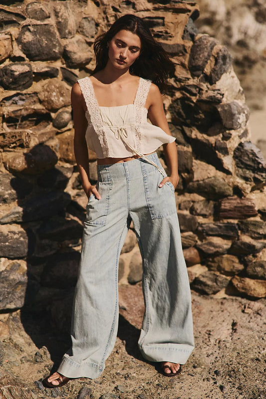 Woman in a white top and light blue jeans standing against a stone wall.