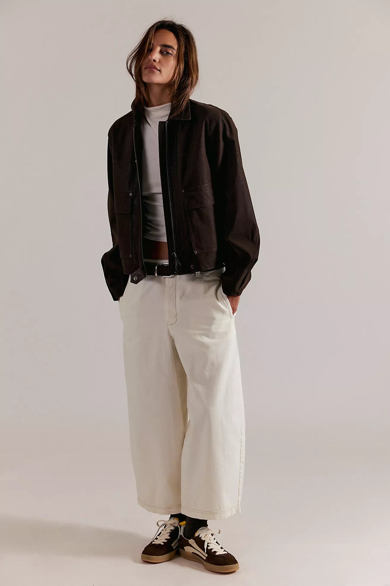 Person wearing a black jacket, white shirt, and white pants on a plain background