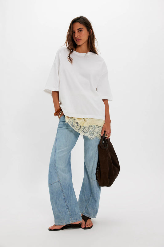 Woman wearing a white top, light blue jeans, and carrying a brown bag on a white background