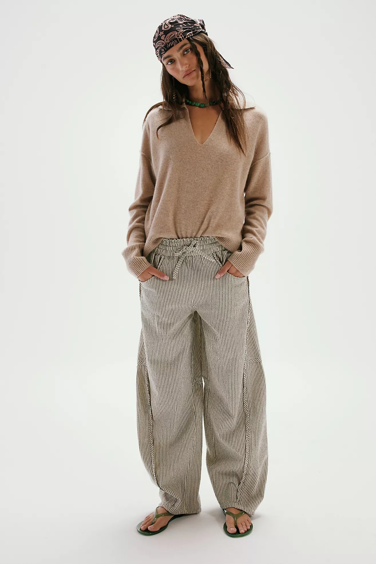 Woman wearing a beige sweater and light-colored pants on a white background