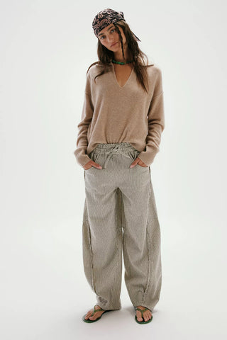 Woman wearing a beige sweater and light-colored pants on a white background