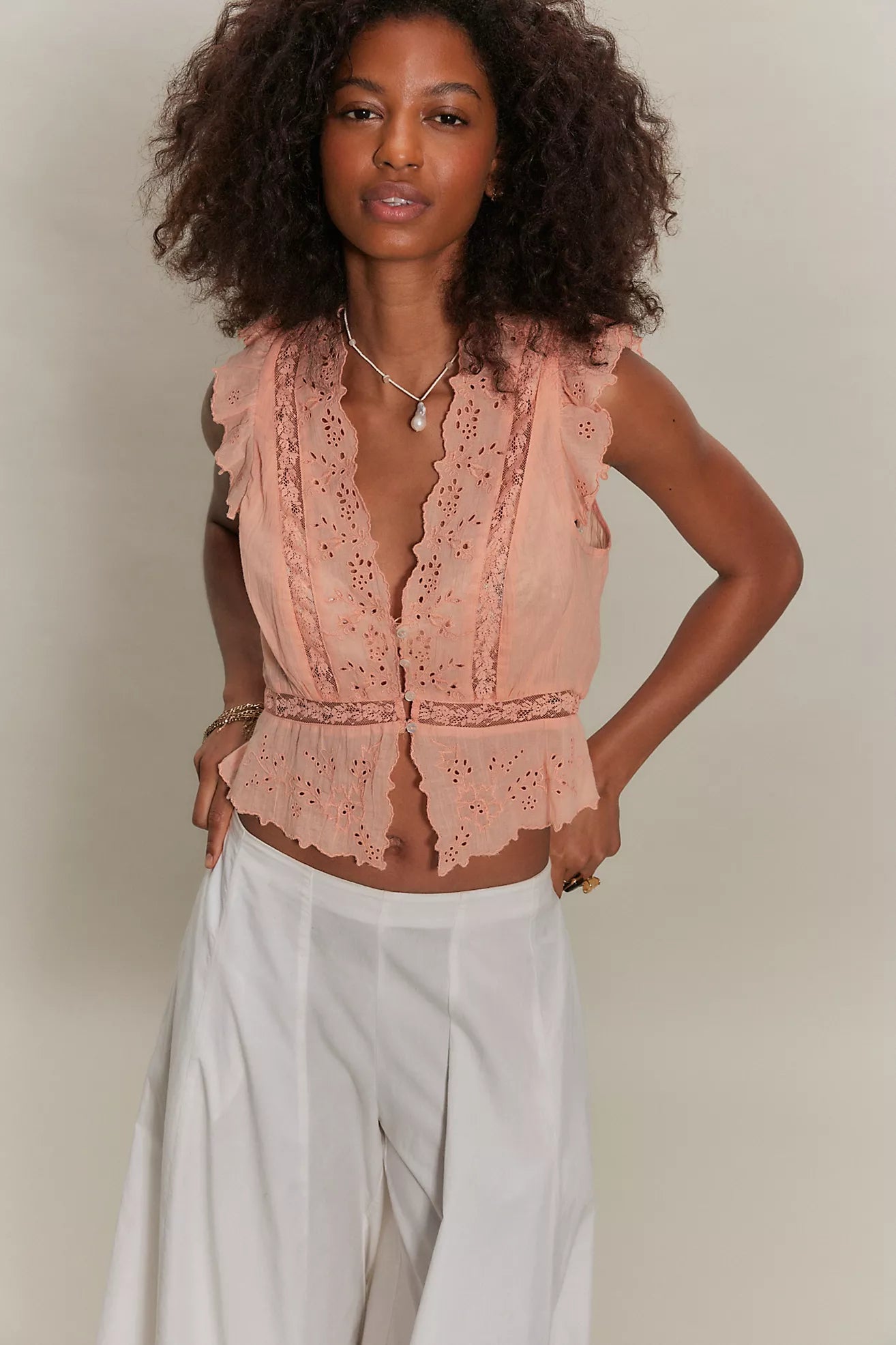 women wearing a peach lace top and white pants. 