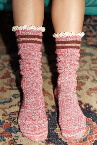 Pink socks with brown stripes and white lace trim worn on a patterned rug.