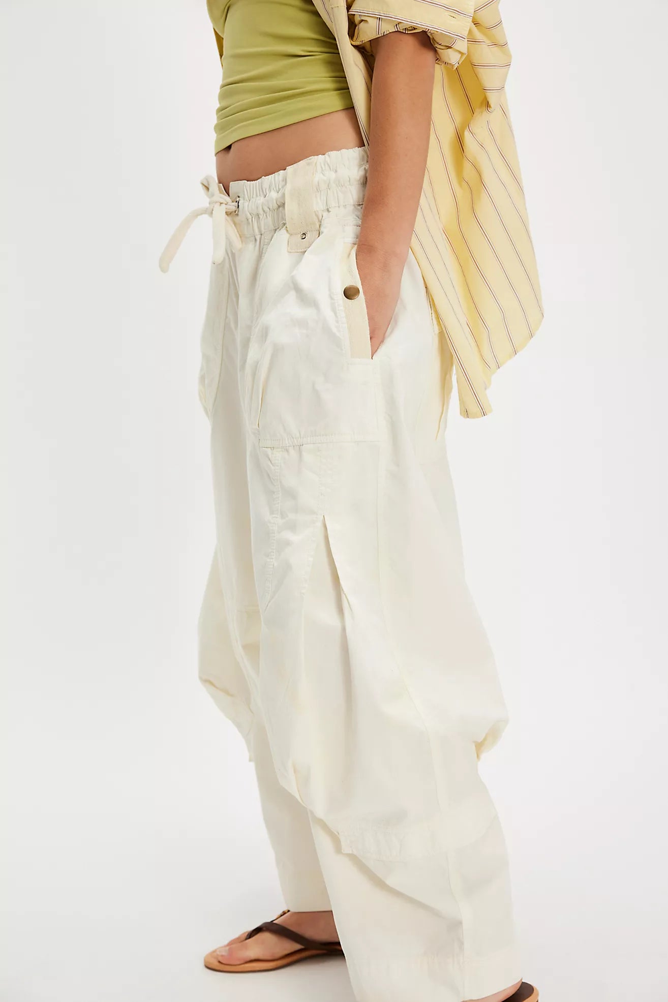 Person wearing white wide-leg pants with a green top and yellow scarf on a white background