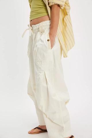 Person wearing white wide-leg pants with a green top and yellow scarf on a white background