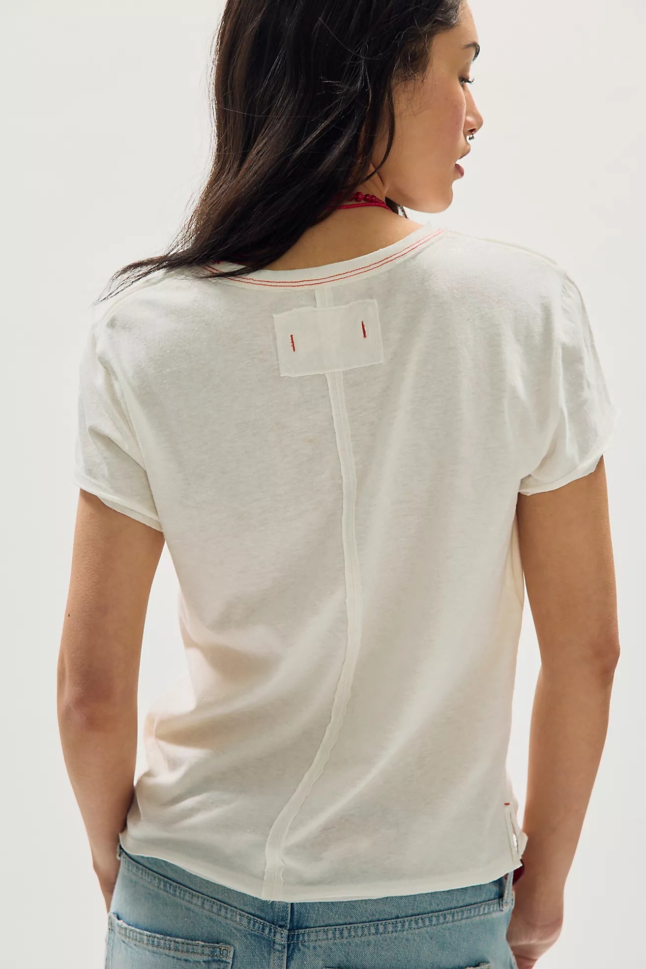 Person wearing a white t-shirt with a brand logo on a plain background
