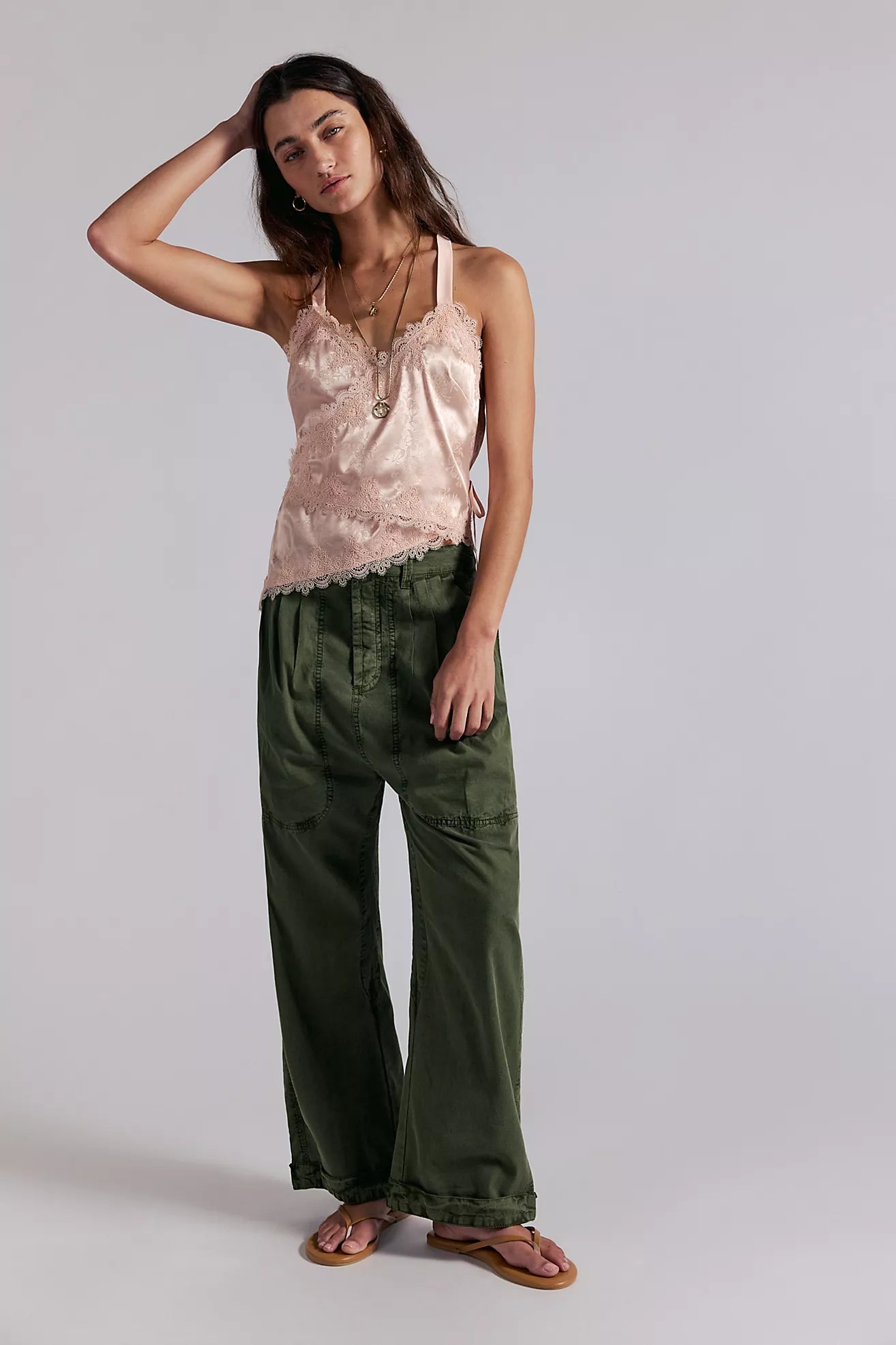 Woman wearing a pink top and green pants against a plain background